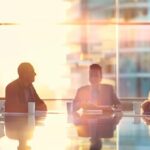 a dynamic office scene showcases a diverse group of engaged professionals gathered around a sleek conference table, animatedly discussing strategies to unlock leadership potential, with modern technology and motivational visuals enhancing the atmosphere.